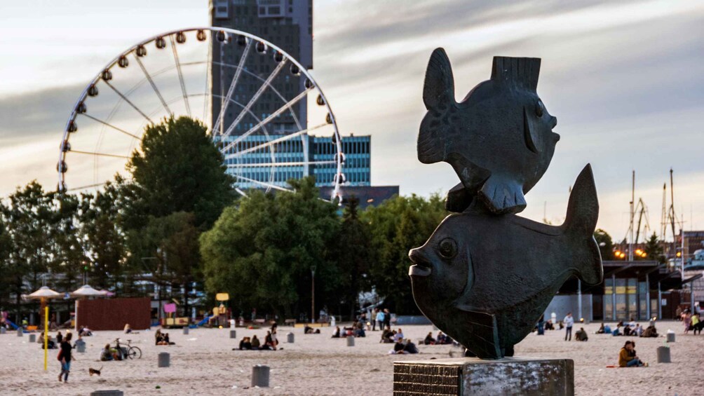 A sculpture of a fish on a pedestal, a Ferris wheel, and a sandy park area with people and trees. 2
