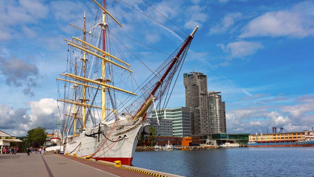 A tall ship docked at a harbor with modern buildings in the background. 1