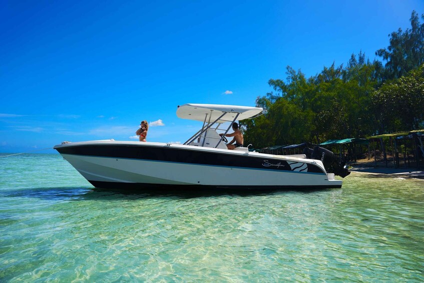 A white motorboat with a canopy on a clear blue sea, surrounded by trees and a sandy beach. 4