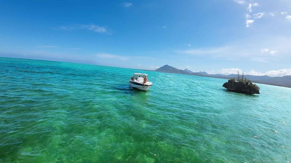 A boat on turquoise water with a rocky outcrop and mountains in the background. 2