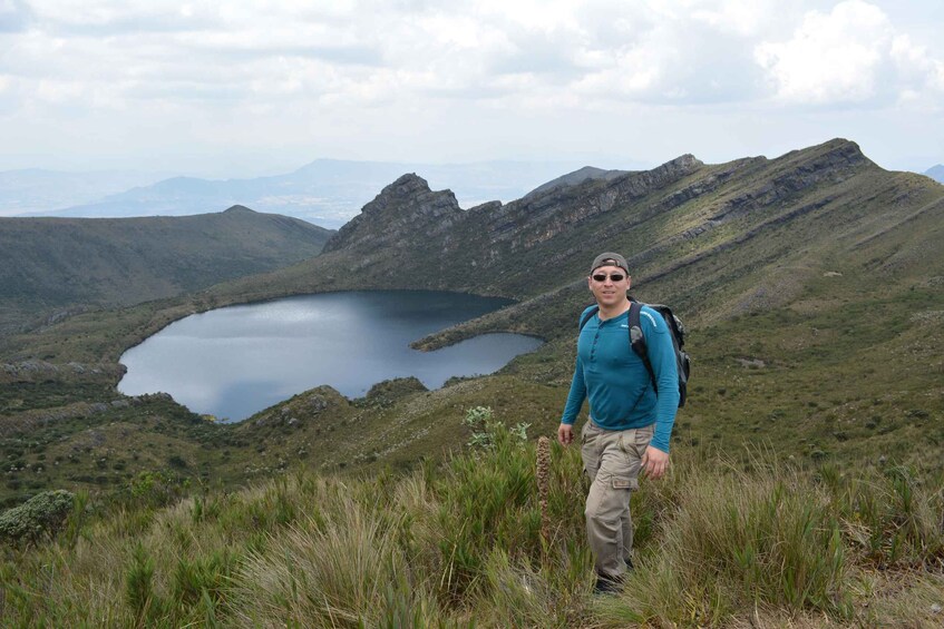 A hiker on a grassy hill with a lake and mountains in the background. 3