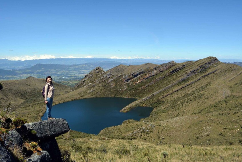 A hiker standing on a rock overlooking a lake surrounded by hills. 1