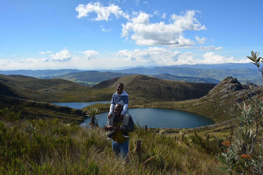 A person carrying a child on their back, overlooking a lake surrounded by hills and mountains. 5