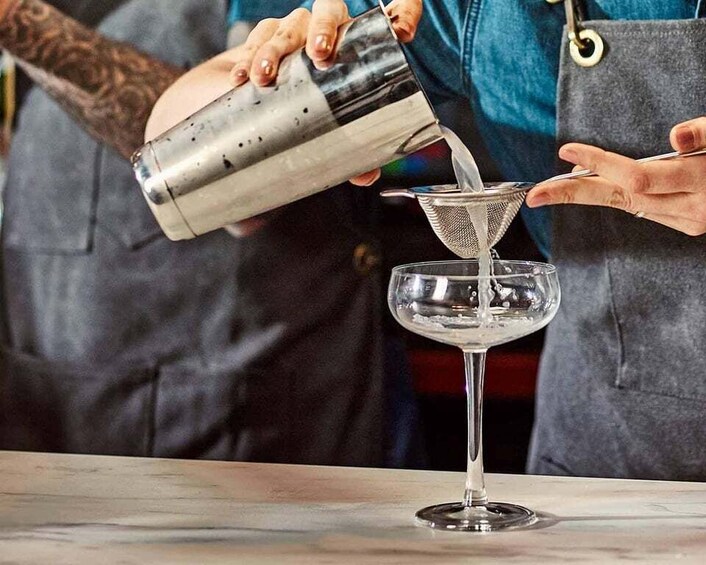 A person pouring a liquid from a shaker into a strainer over a glass. 1