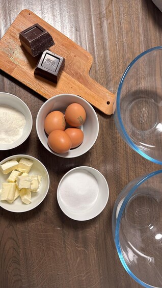 A wooden cutting board with chocolate, eggs, flour, butter, and sugar on a wooden table. 5