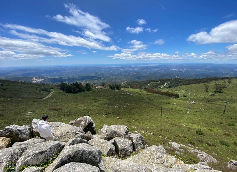 A mountainous landscape with a clear sky, rocky foreground, and a distant view of valleys and towns. 3