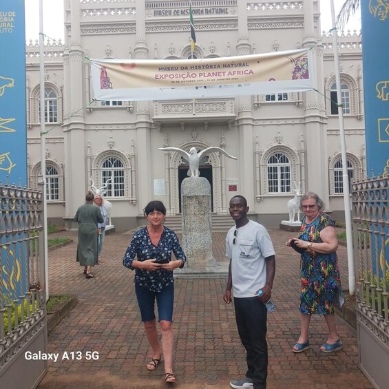 A historic building with ornate architecture, a banner for the Museu da História Natural Exposição Planet Africa, and a statue of an eagle. 1