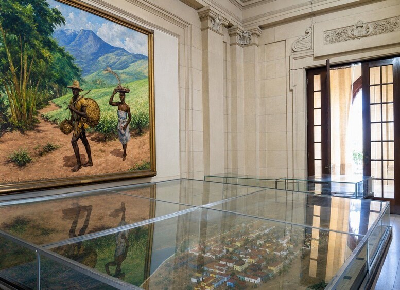 A museum interior with a large painting of two figures in a landscape, a glass display case, and a model town. 2