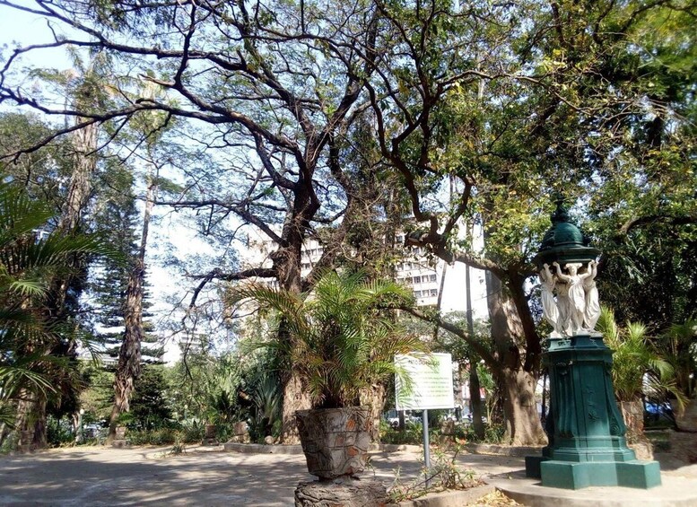 A park with a statue, a stone planter, and a sign. 3