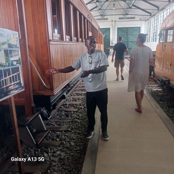A person standing by a wooden structure with a poster, a train track, and a train in the background. 3