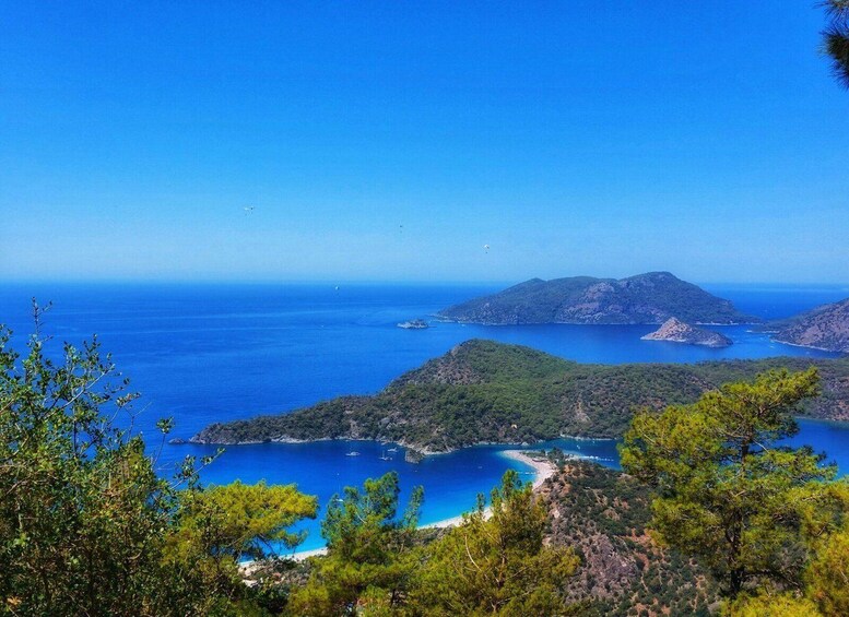 A coastal landscape with clear blue waters, green hills, and a small beach. 1