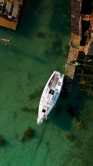 A white boat docked at a pier with clear water and greenery around. 2