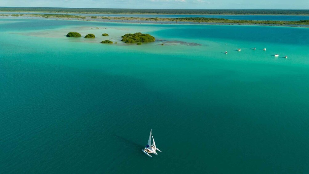 A sailboat in a turquoise sea with a small island with green vegetation. 1