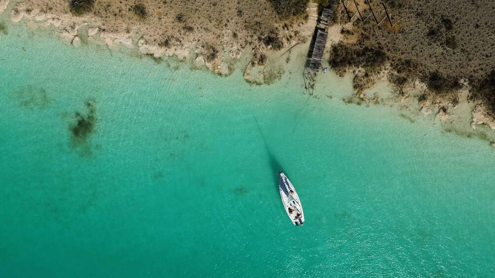 An aerial view of a boat on turquoise waters near a sandy beach with sparse vegetation. 4