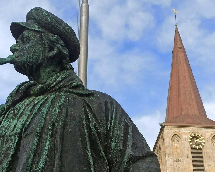 A statue of a man with a pipe, a church steeple, and a clock tower in the background. 2