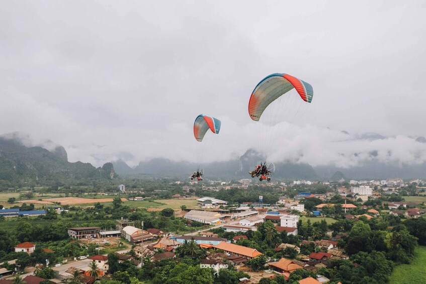 Paragliders flying over a town with mountains in the background. 1