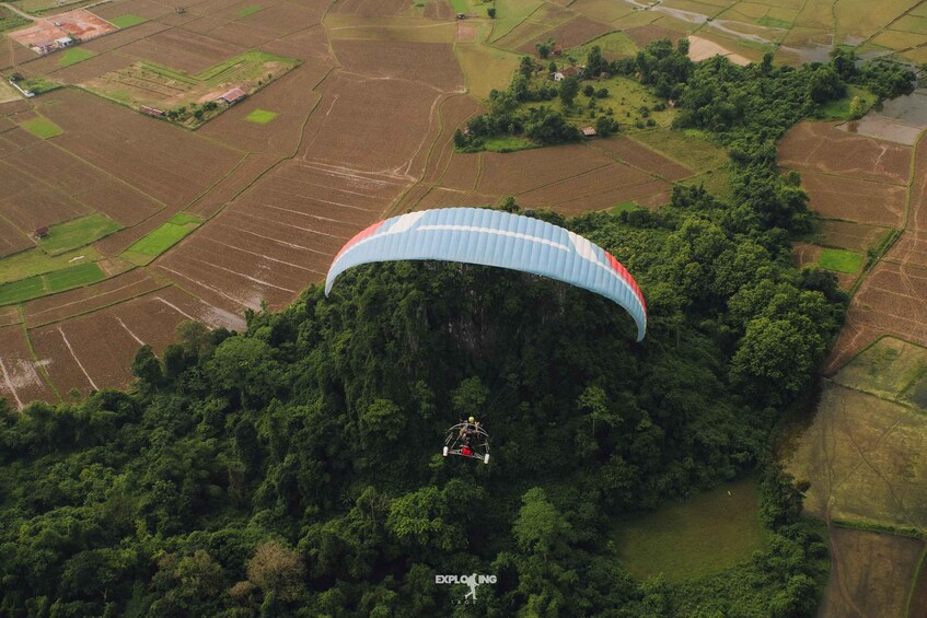 A paraglider descending towards a forested area with agricultural fields. 3