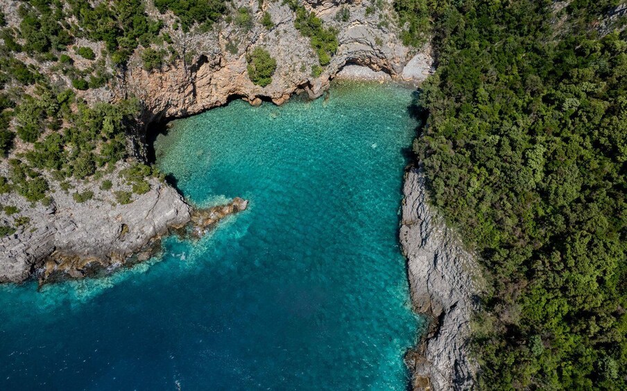 A coastal landscape with a clear turquoise sea, rocky cliffs, and dense green vegetation. 4