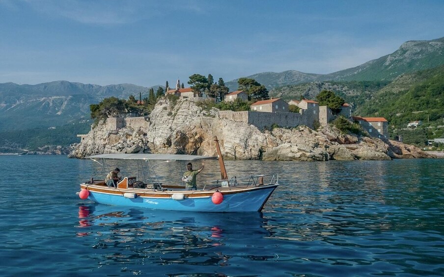A boat on calm water near a rocky coastline with houses on a hill. 1