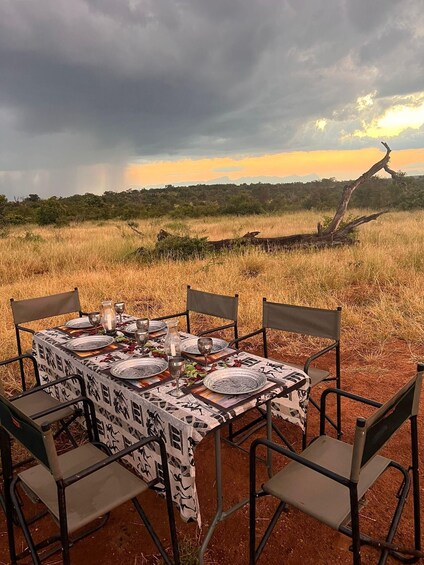 A table set outdoors with chairs, surrounded by a grassy field and a sunset in the background. 3