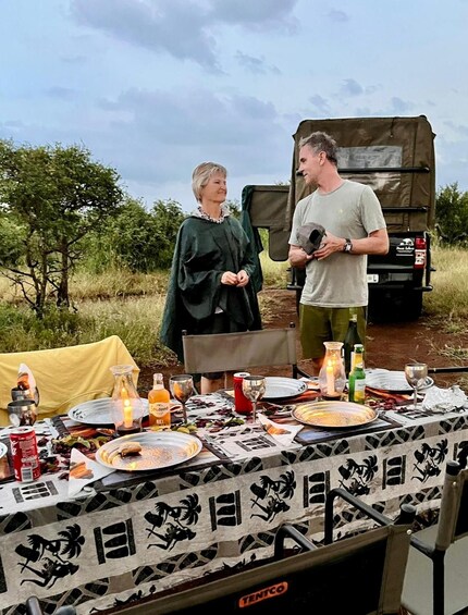 Two people standing by a table set outdoors with a vehicle in the background. 2