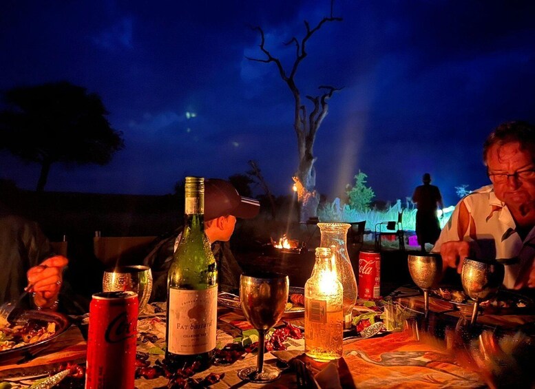 An outdoor dining area with a table set for a meal, featuring a bottle of wine, a glass, a can of soda, and a lit candle. 5