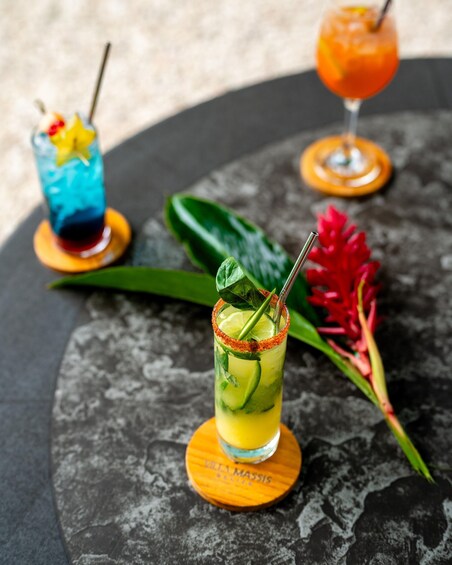 Three cocktails on wooden coasters with tropical garnishes. 5