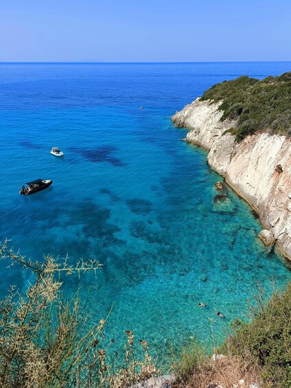 A coastal landscape with clear blue waters, rocky cliffs, and boats. 1