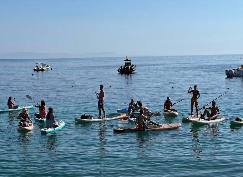 People paddleboarding on calm waters with boats in the background. 3