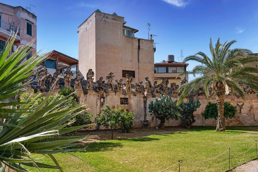 A courtyard with a statue of soldiers, palm trees, and buildings in the background. 3