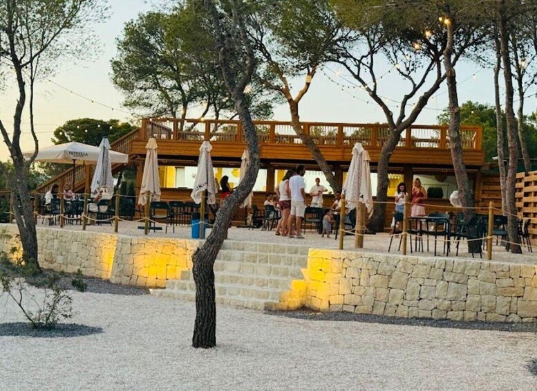 A wooden outdoor dining area with tables and umbrellas, surrounded by trees and a stone wall. 3