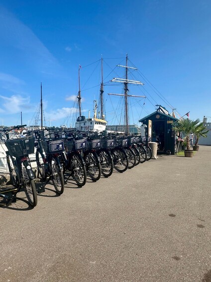 A row of bicycles parked in a marina with a tall ship in the background. 3