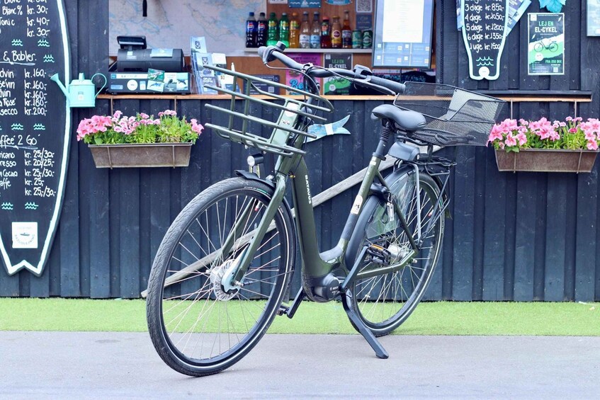 A green bicycle with a basket and a water bottle attached, parked in front of a blackboard with a menu listing prices. 5