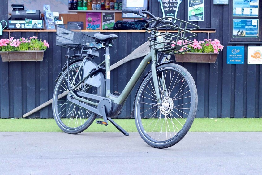 A stationary bicycle with a basket and kickstand, parked in front of a store with a wooden counter and flower boxes. 2