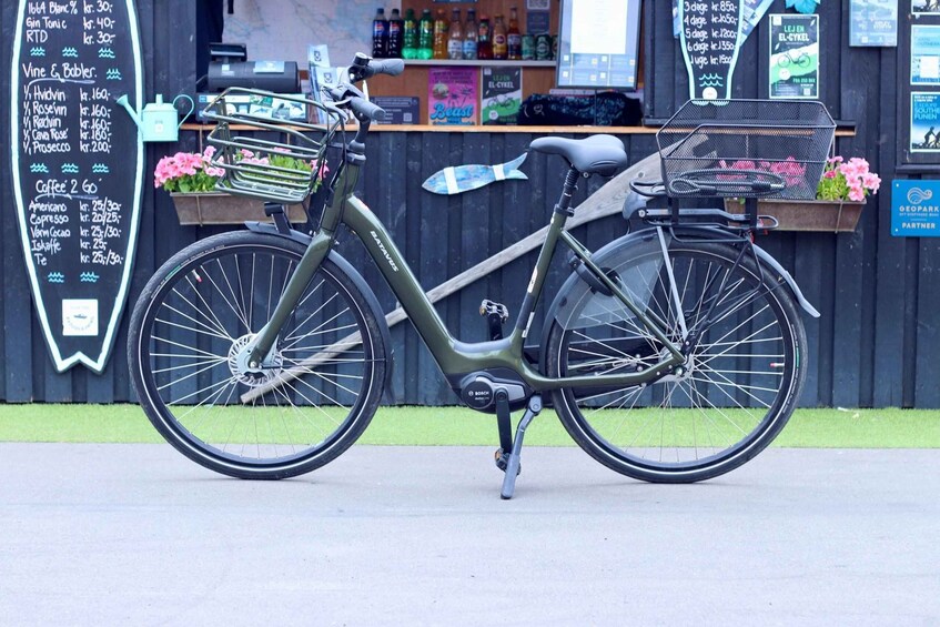 A green bicycle with a basket and a water bottle, parked in front of a shop with a chalkboard menu. 4