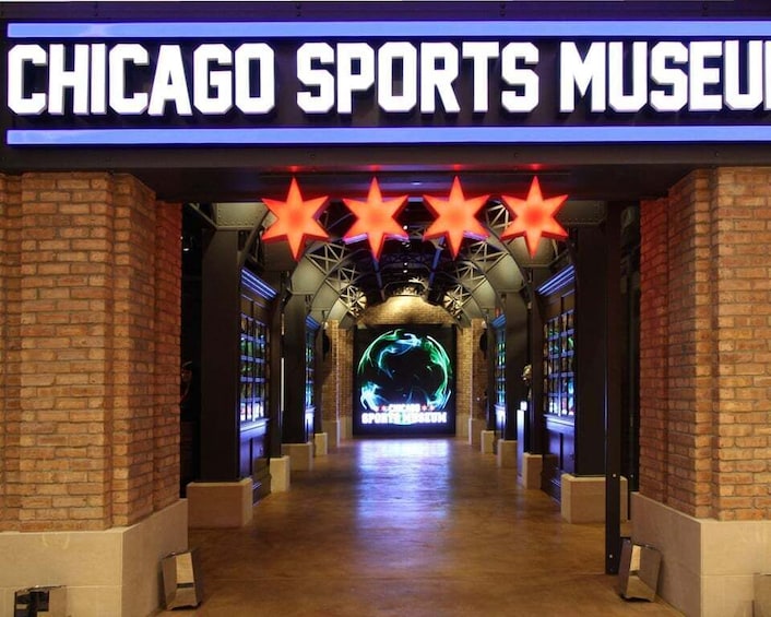 The entrance to the Chicago Sports Museum with a brick facade, a neon sign, and a central display featuring a sports-related graphic. 1