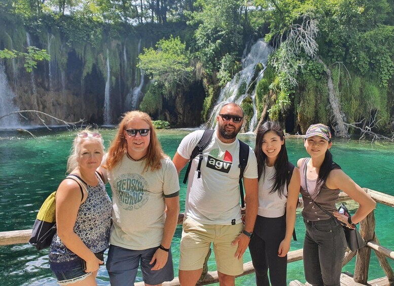 A group of people standing by a clear, turquoise body of water with a waterfall in the background. 3
