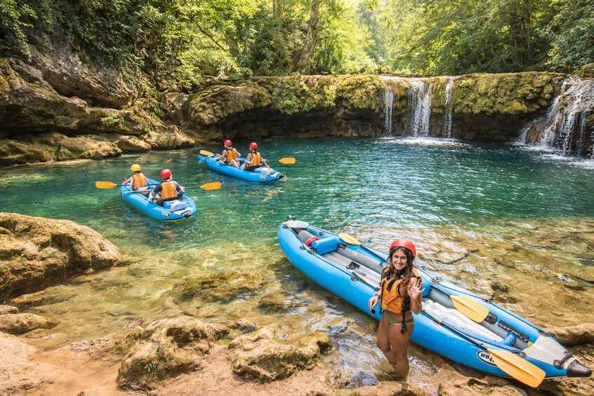 A clear river with kayaks and a waterfall. 1