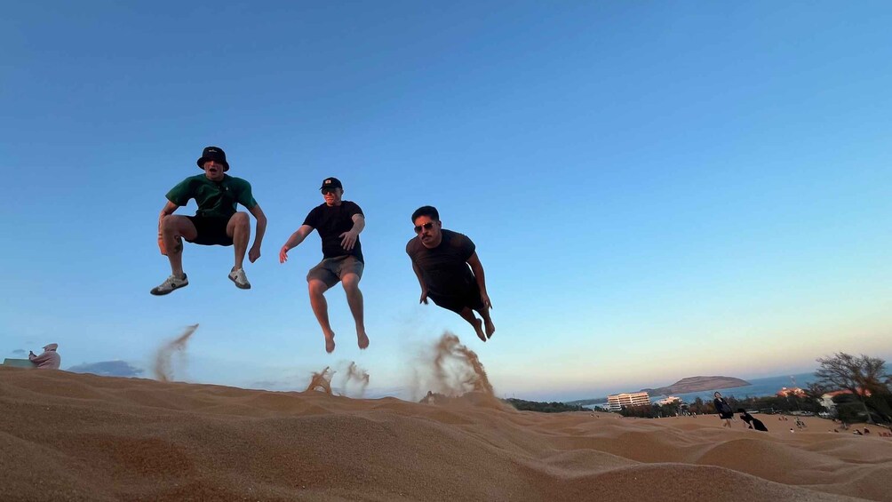 Three people jumping off a sand dune into the air. 5