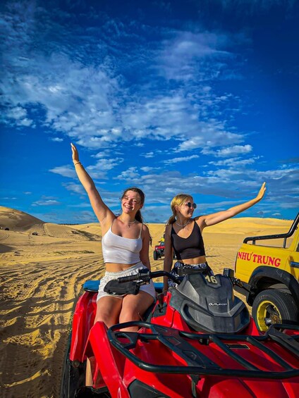Two people on a red ATV with a yellow vehicle in a desert landscape. 2