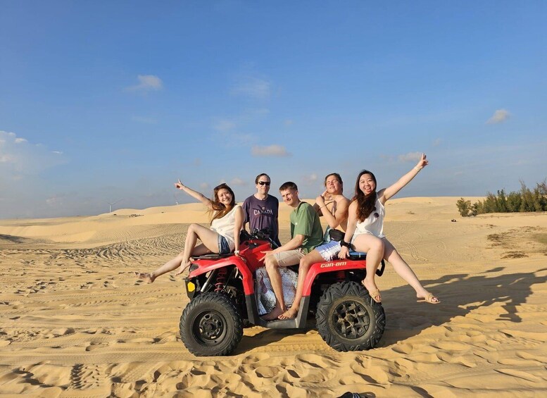 A group of people on a red ATV in a desert with sand dunes and a clear sky. 4