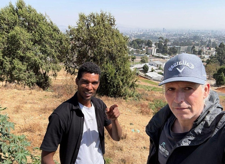 Two people standing on a hill with a cityscape in the background. 2