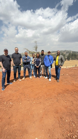 A group of people standing on a dirt ground with a hilly landscape and trees in the background. 5