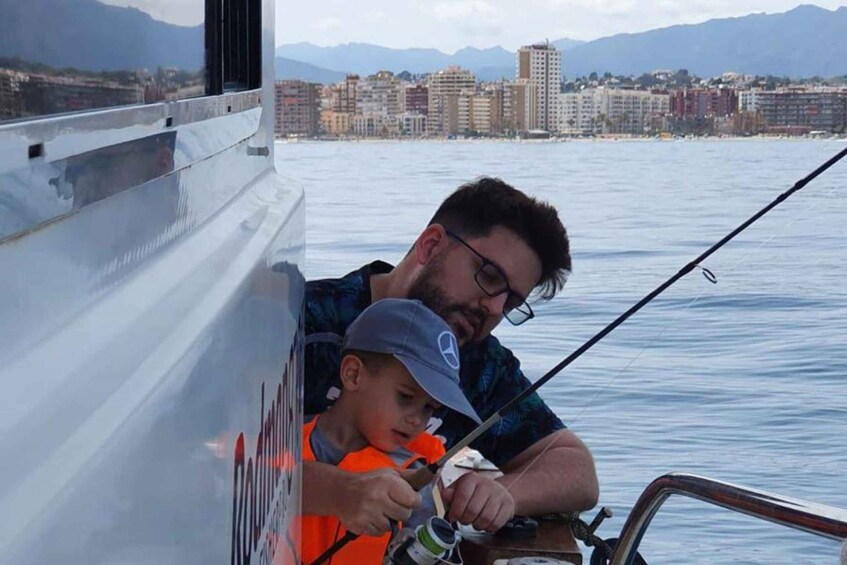 A man and a child fishing on a boat with a cityscape and mountains in the background. 5