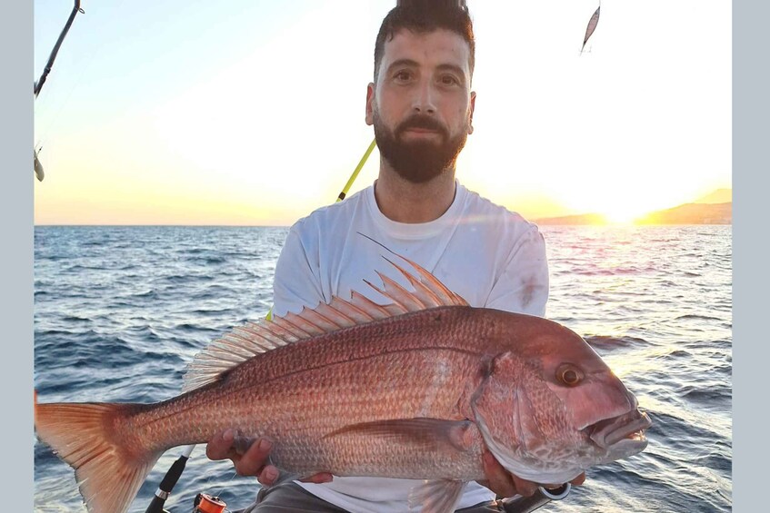 A person holding a large fish on a boat with a sunset in the background. 3