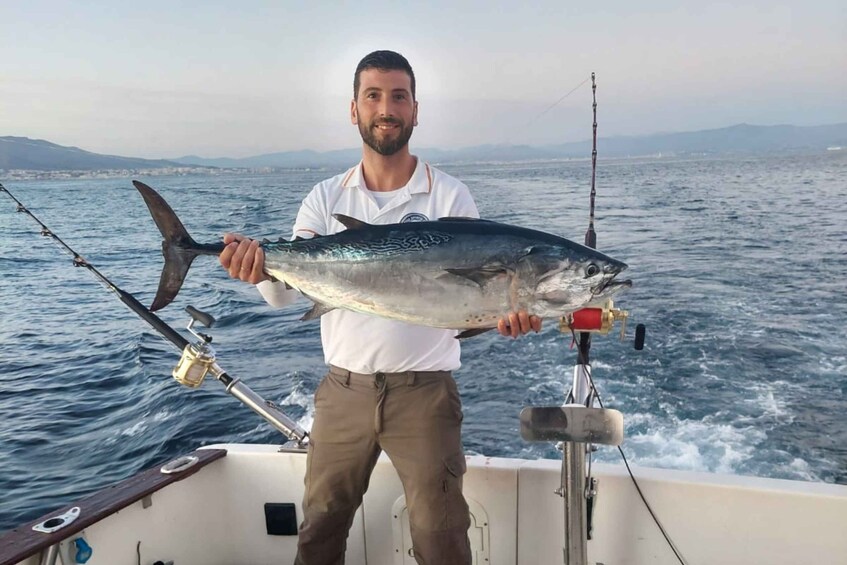 A person holding a large fish on a boat with a fishing rod in the background. 1