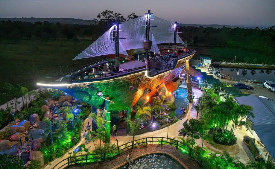 A large, illuminated ship-themed attraction with a waterfall and tropical landscaping. 1