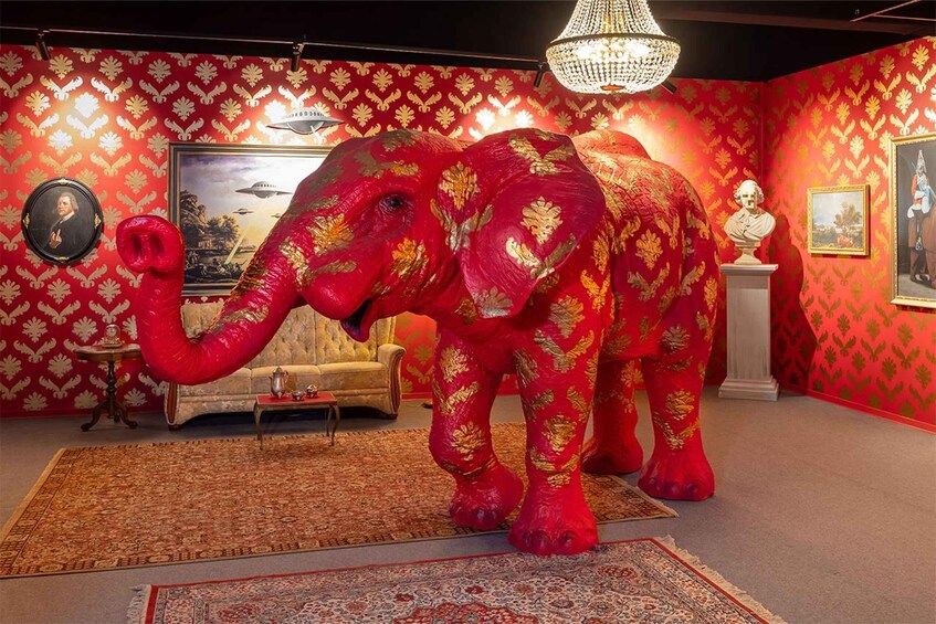 A room with a large red and gold elephant statue, a chandelier, and a sofa. 1
