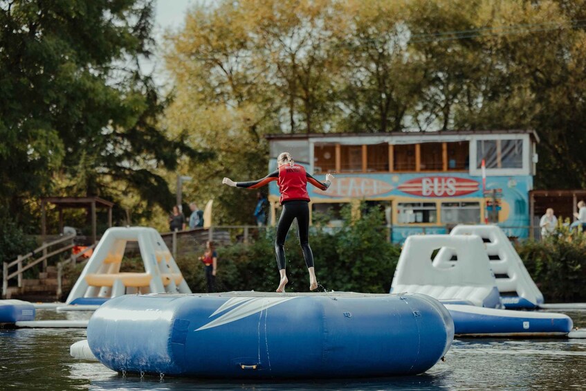 A person jumping off a blue inflatable structure in a body of water with a bus and a building labeled 'BUS' in the background. 2
