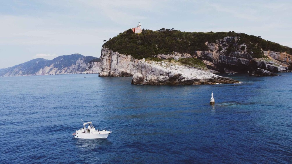A boat on calm sea waters, a rocky island with a lighthouse, and distant mountains. 1
